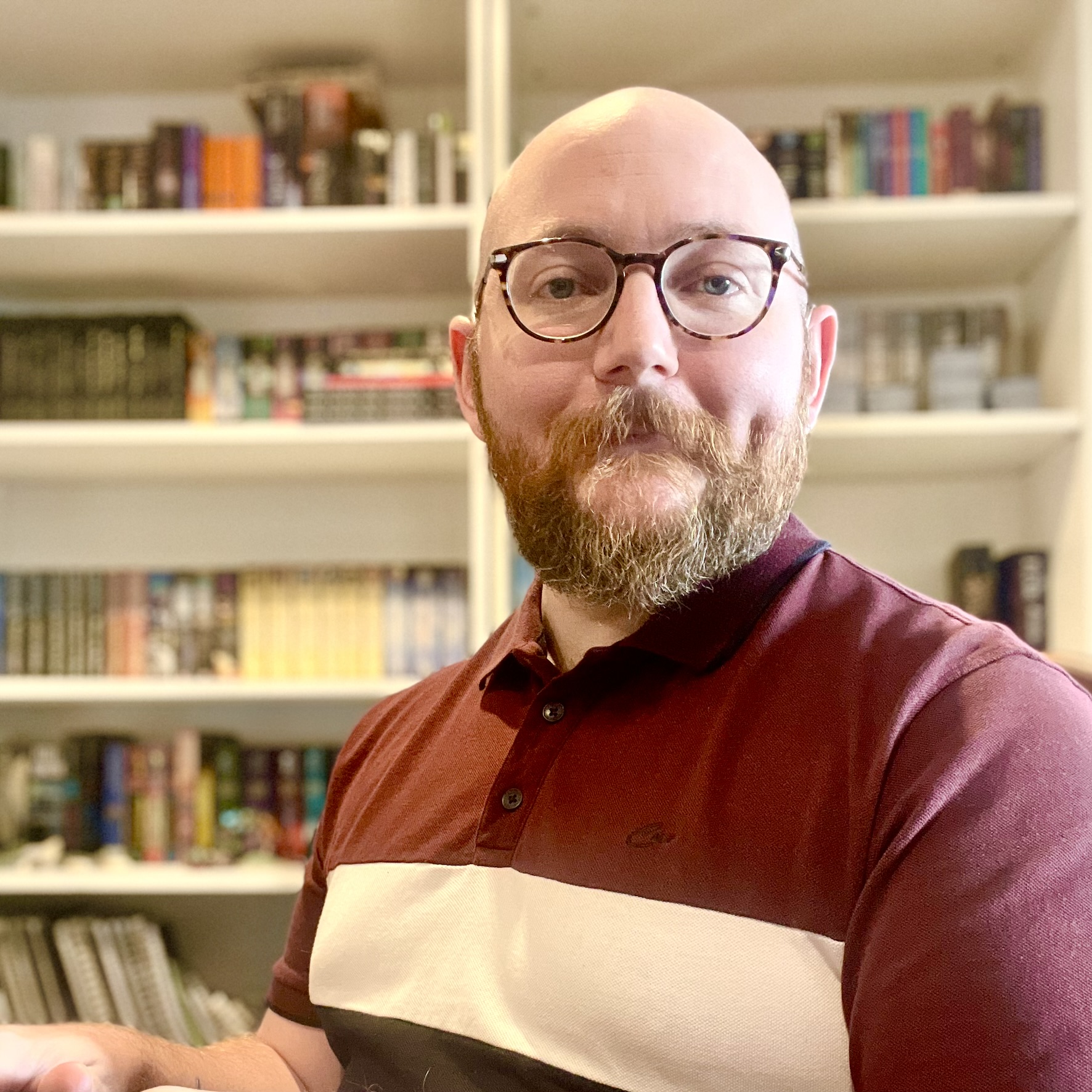 Jesse, smiling, wearing glasses and a maroon polo shirt, sitting in front of a bookshelf